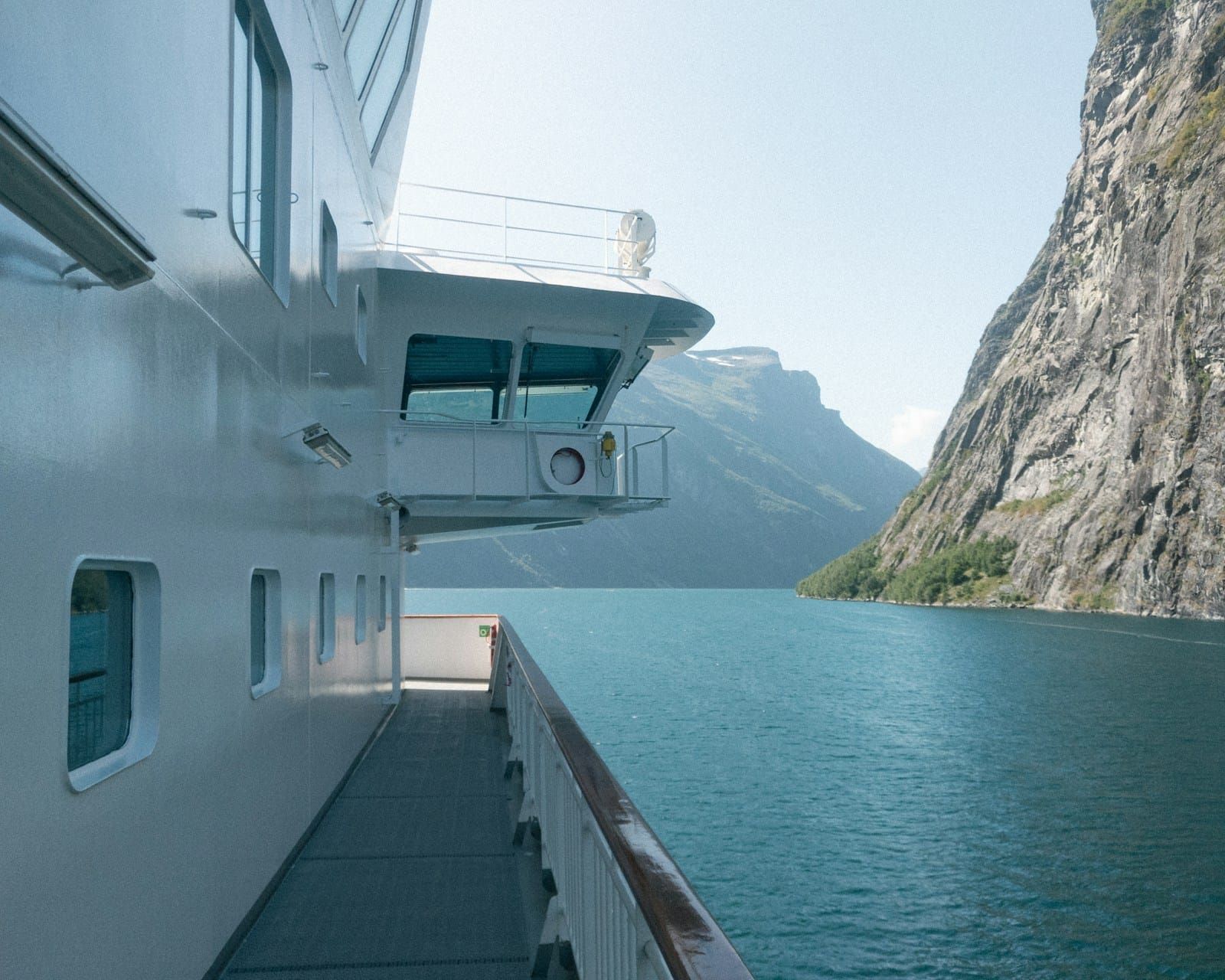 Looking along the side deck of a ship as it sails between sheer rock walls into a calm Norwegian fjord